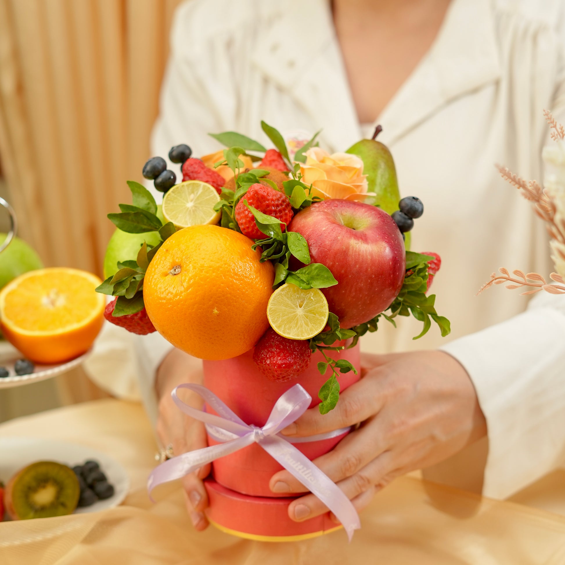 Bouquet made of fruits and flowers held by a person, with a focus on oranges, apples, and other fruits.