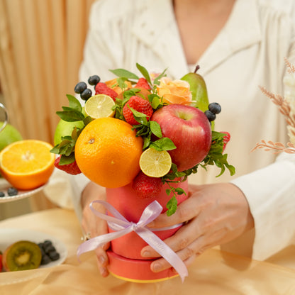 Bouquet made of fruits and flowers held by a person, with a focus on oranges, apples, and other fruits.