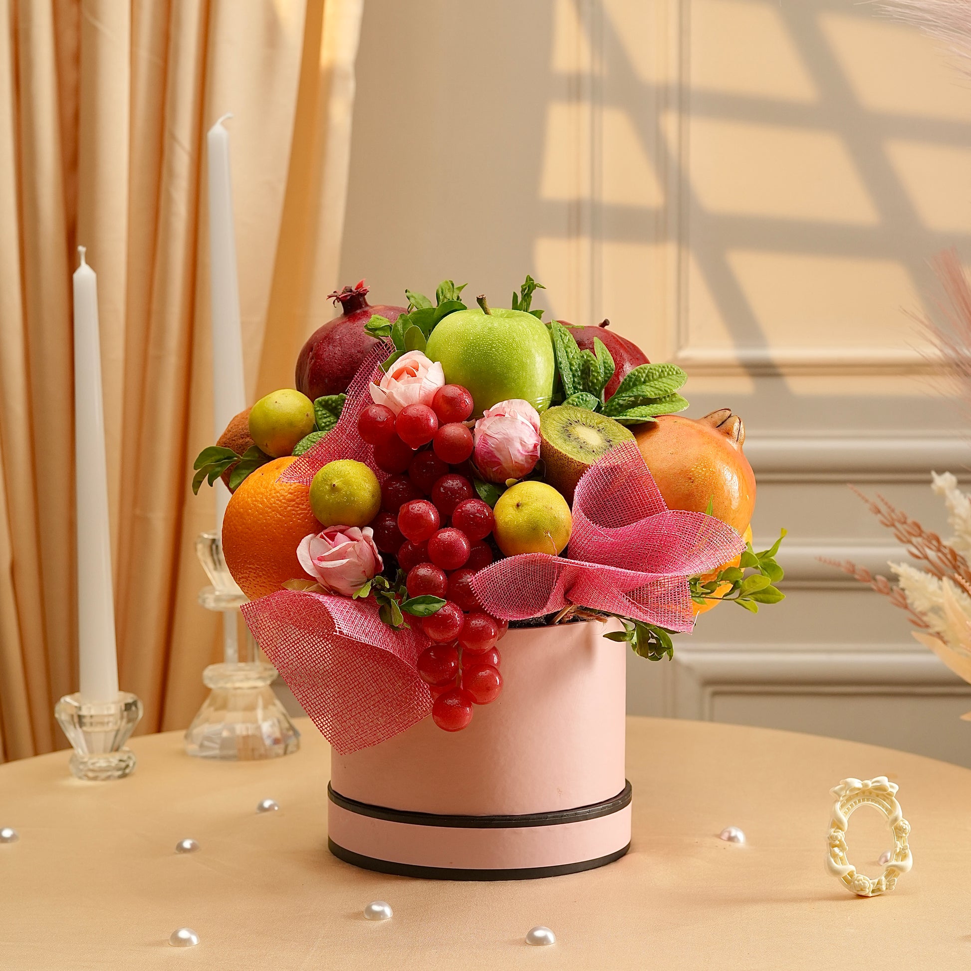 Fruit arrangement in a pink container with decorative ribbons on a table.