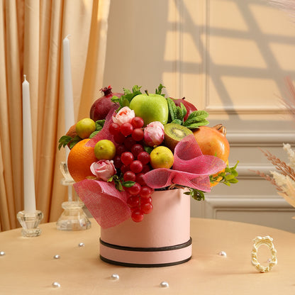 Fruit arrangement in a pink container with decorative ribbons on a table.