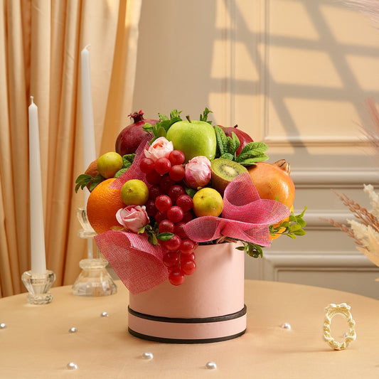 Fruit arrangement in a pink container with decorative ribbons on a table.