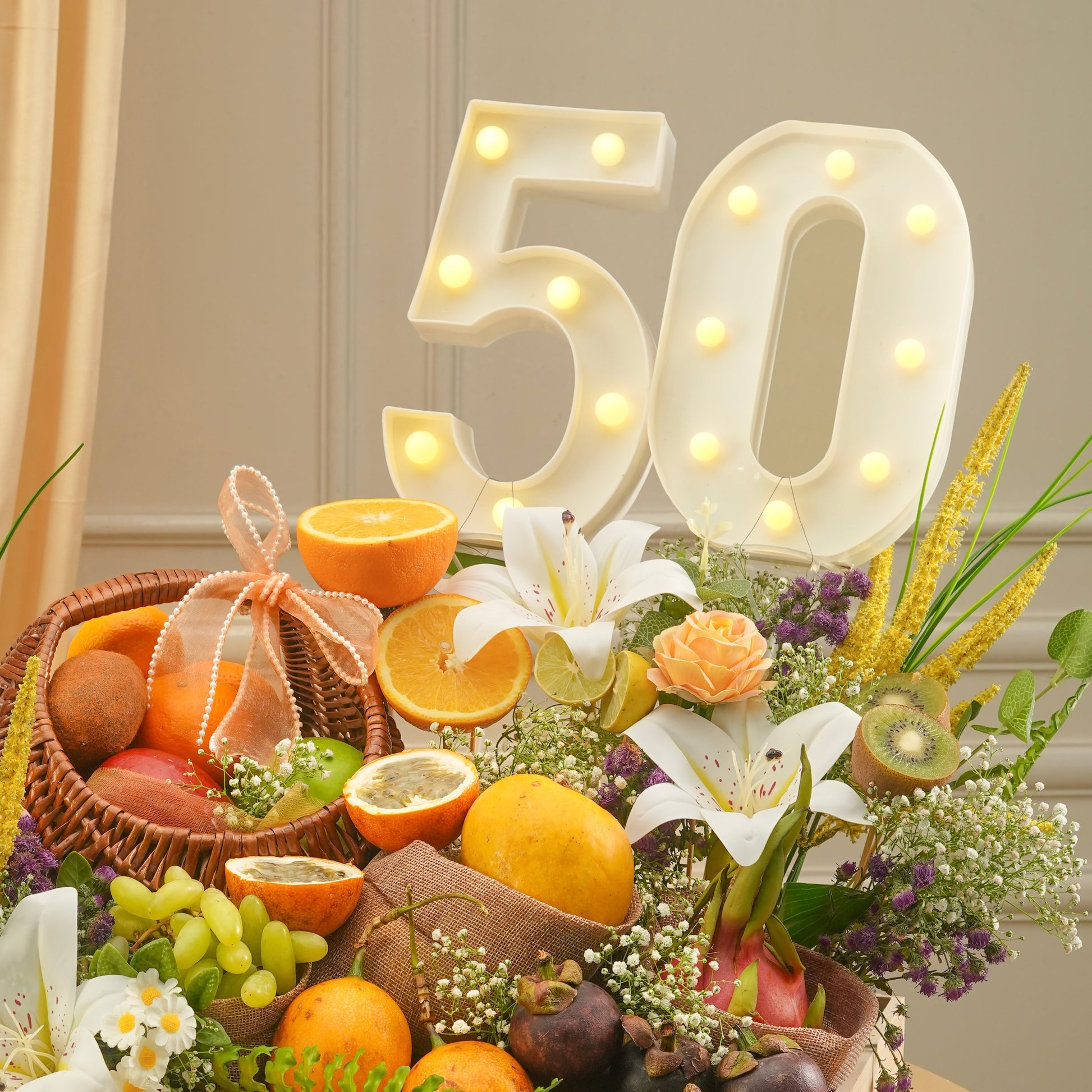 Decorative setup with fruit basket, flowers, and illuminated number '50' on a neutral background