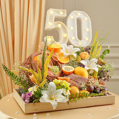 Decorative table setup with flowers, fruits, and a '50' sign on a wooden tray.