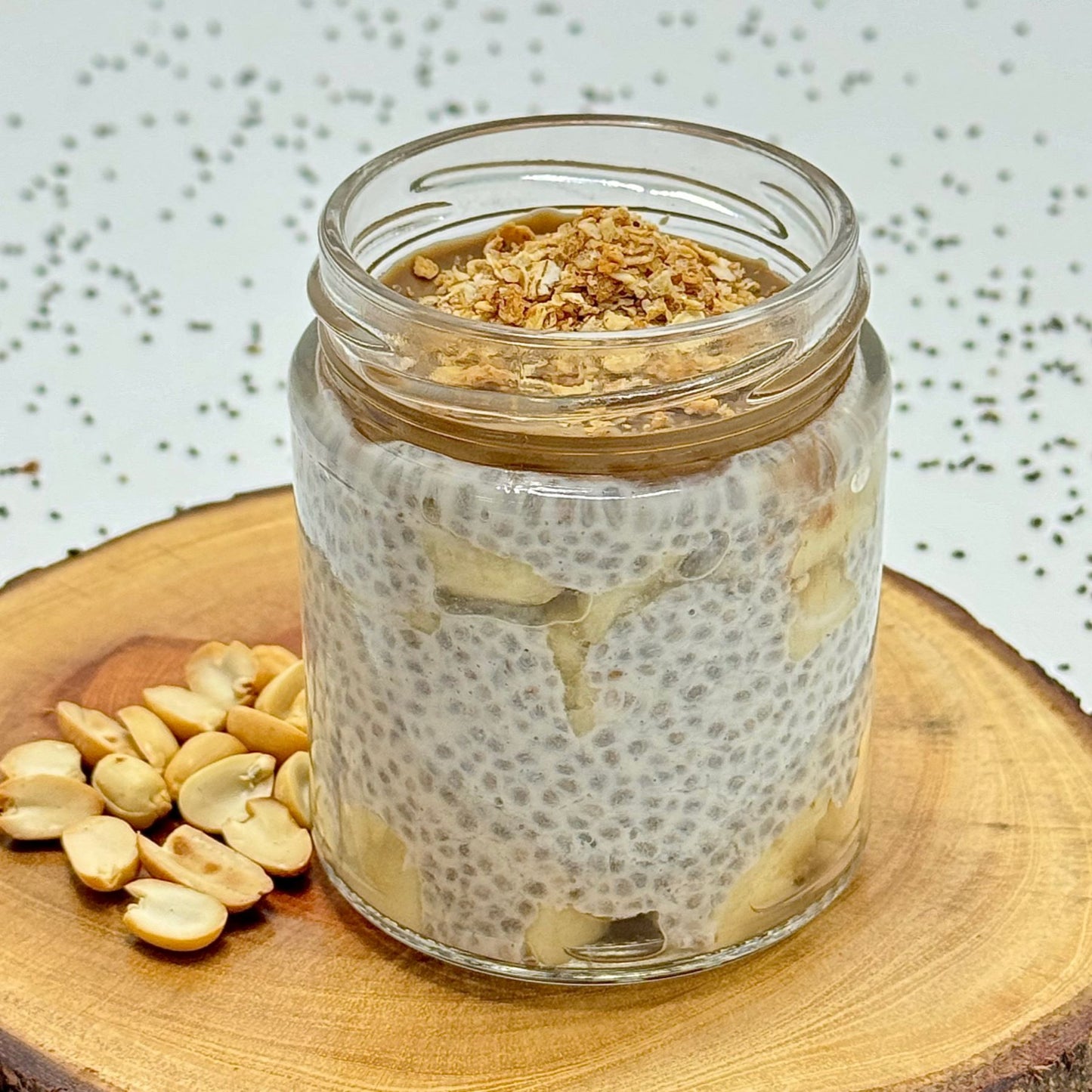 Glass jar of chia pudding with peanuts on a wooden surface