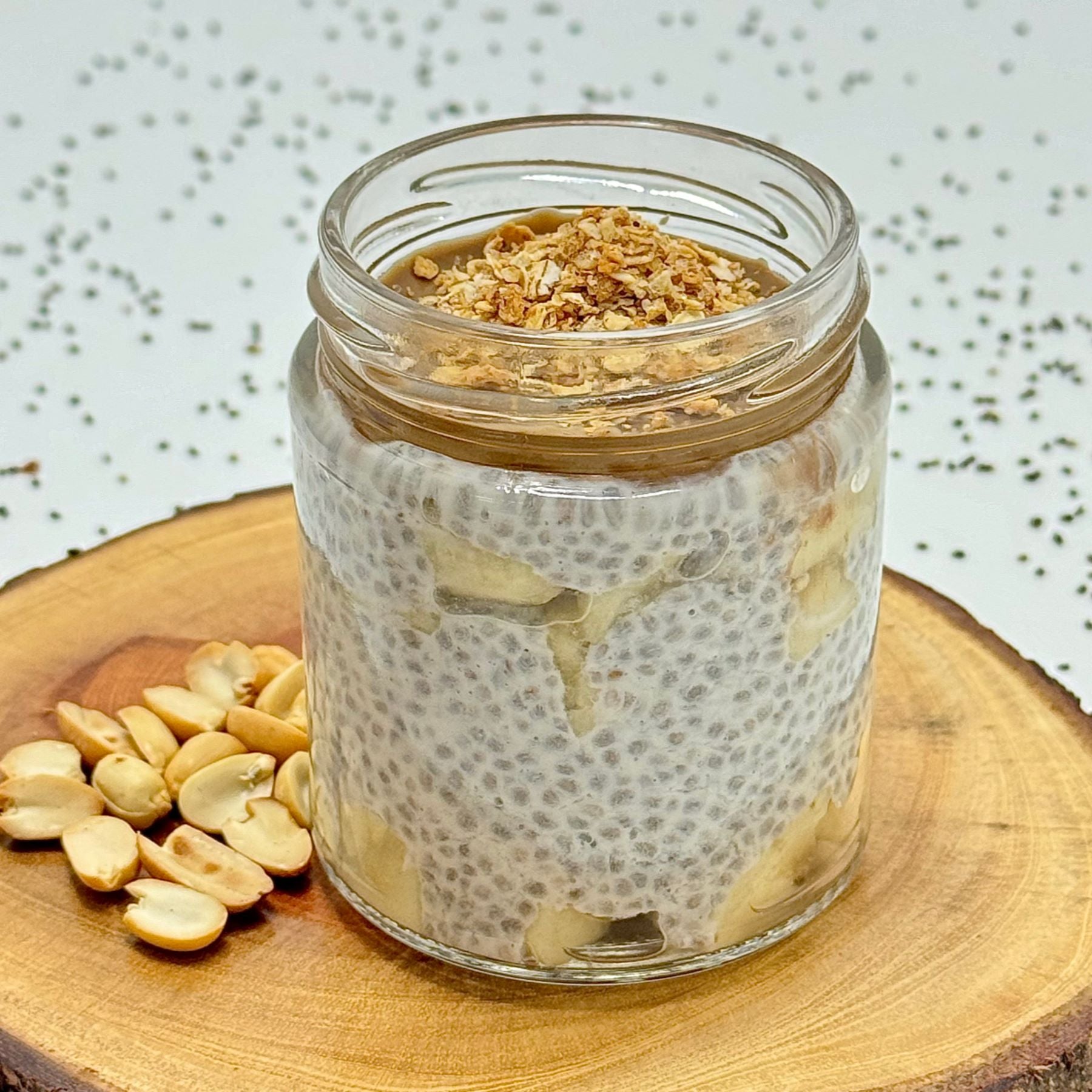 Glass jar of chia pudding with peanuts on a wooden surface