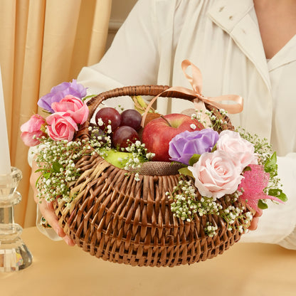 Person holding a wicker basket with fruits and flowers on a beige background