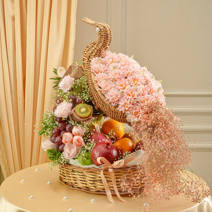 Decorative basket with flowers, fruits, and a bow on a table.