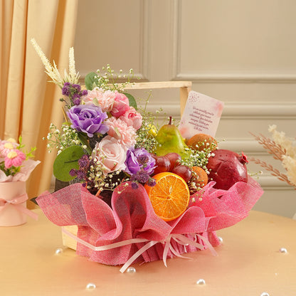 Decorative fruit and flower arrangement with pink ribbon on a table.